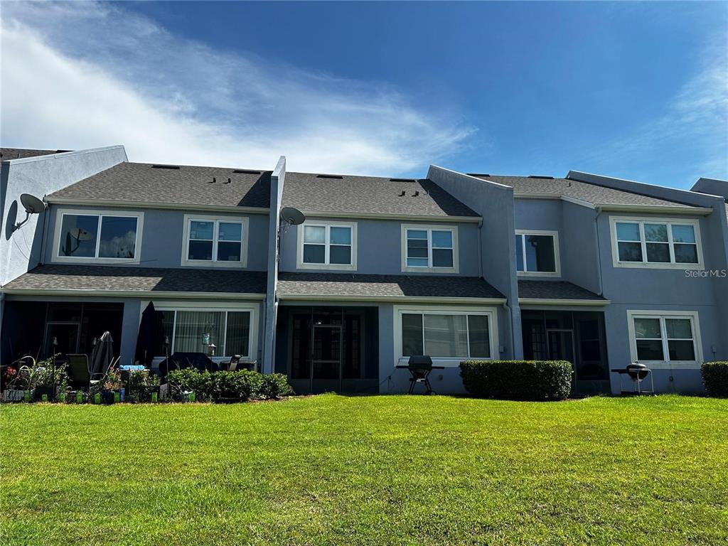 The rear exterior of a multi-unit townhouse complex features gray siding, shingled roofs, and grassy yards — 1969 CHATHAM PLACE DRIVE, ORLANDO, FL