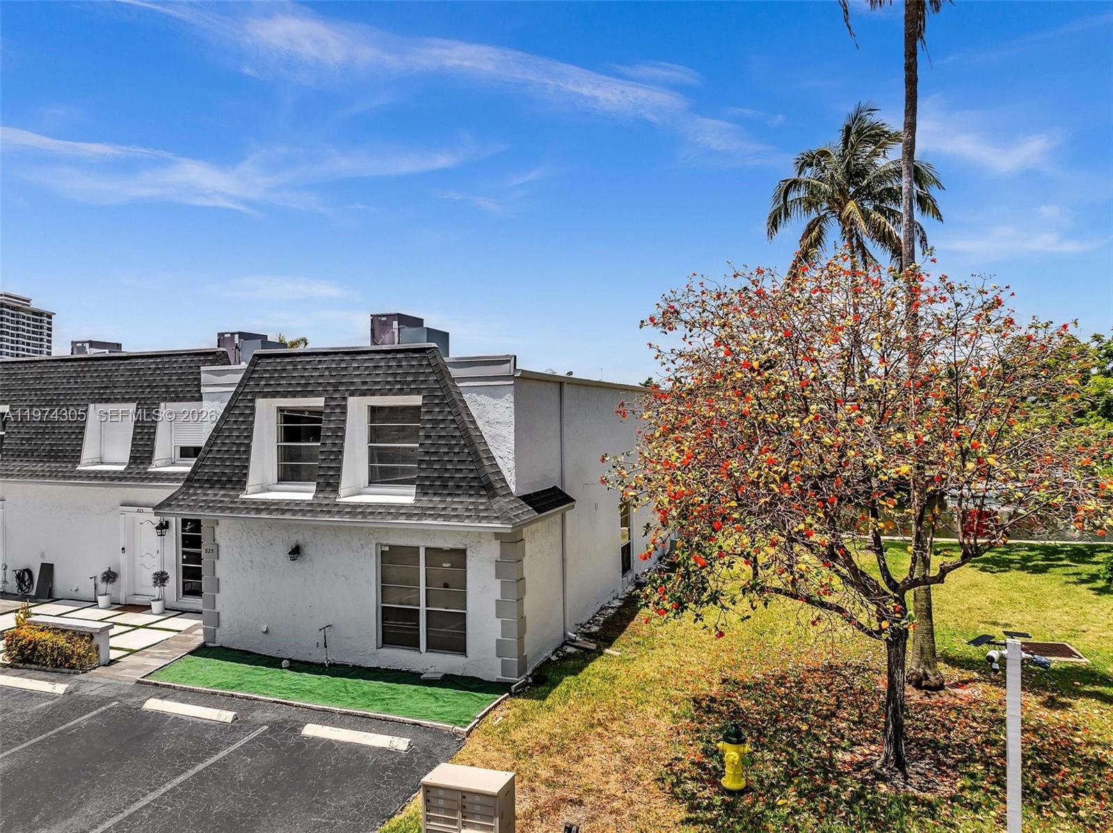 A two-story townhouse with a mansard roof stands next to a tree with orange leaves — 825 NE 26th Ave, Hallandale Beach FL 33009, HALLANDALE BEACH, FL