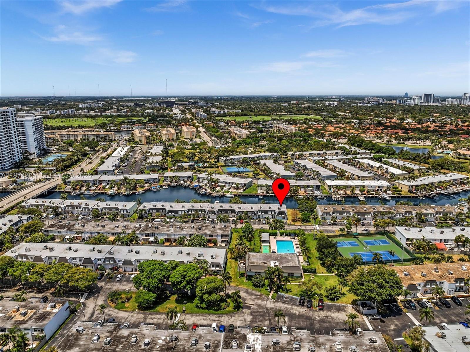 An aerial view shows a residential complex with a canal, swimming pool, and tennis courts — 825 NE 26th Ave, Hallandale Beach FL 33009, HALLANDALE BEACH, FL