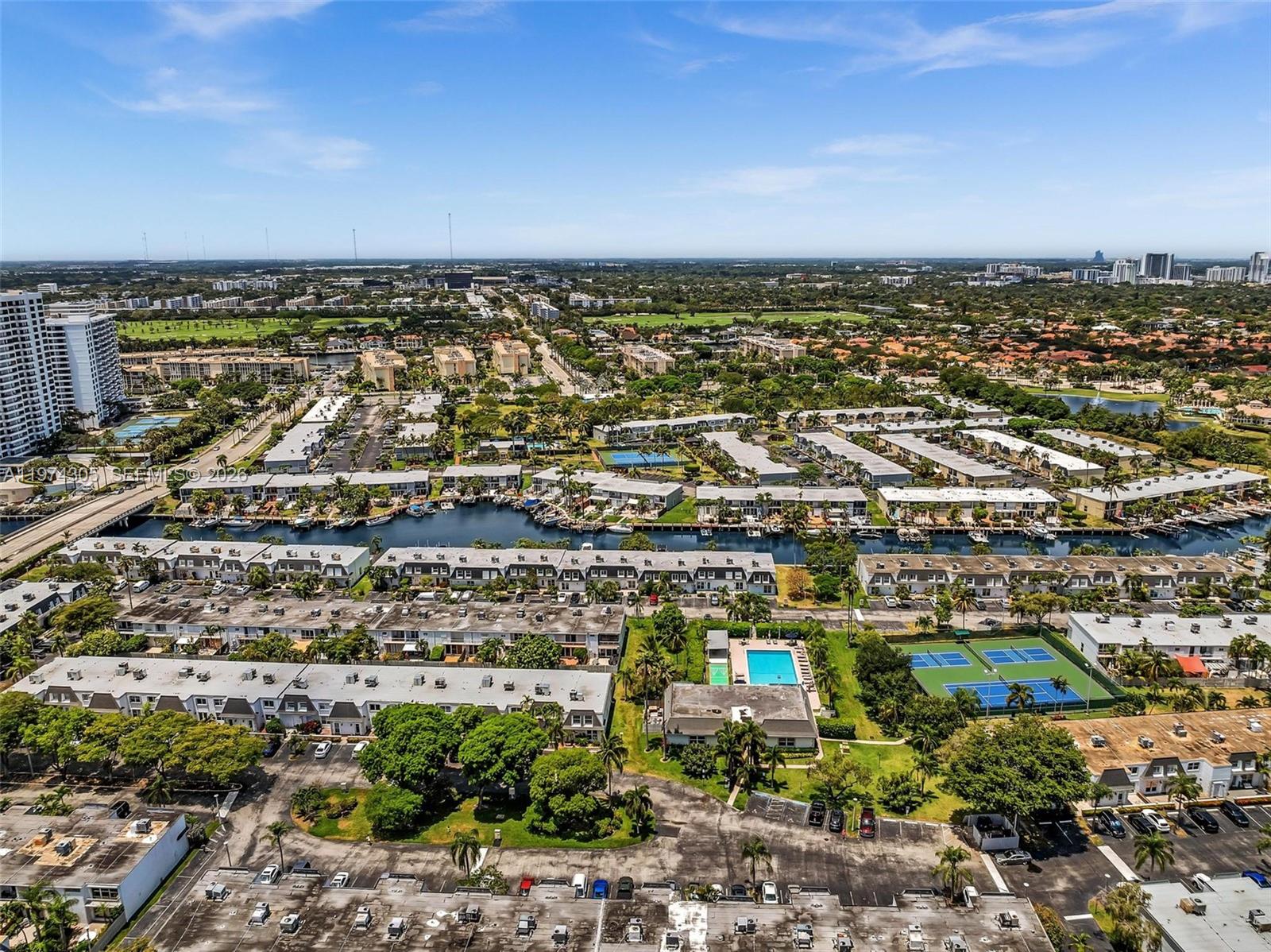 An aerial view shows a residential complex with a canal, swimming pool, and tennis courts — 825 NE 26th Ave, Hallandale Beach FL 33009, HALLANDALE BEACH, FL
