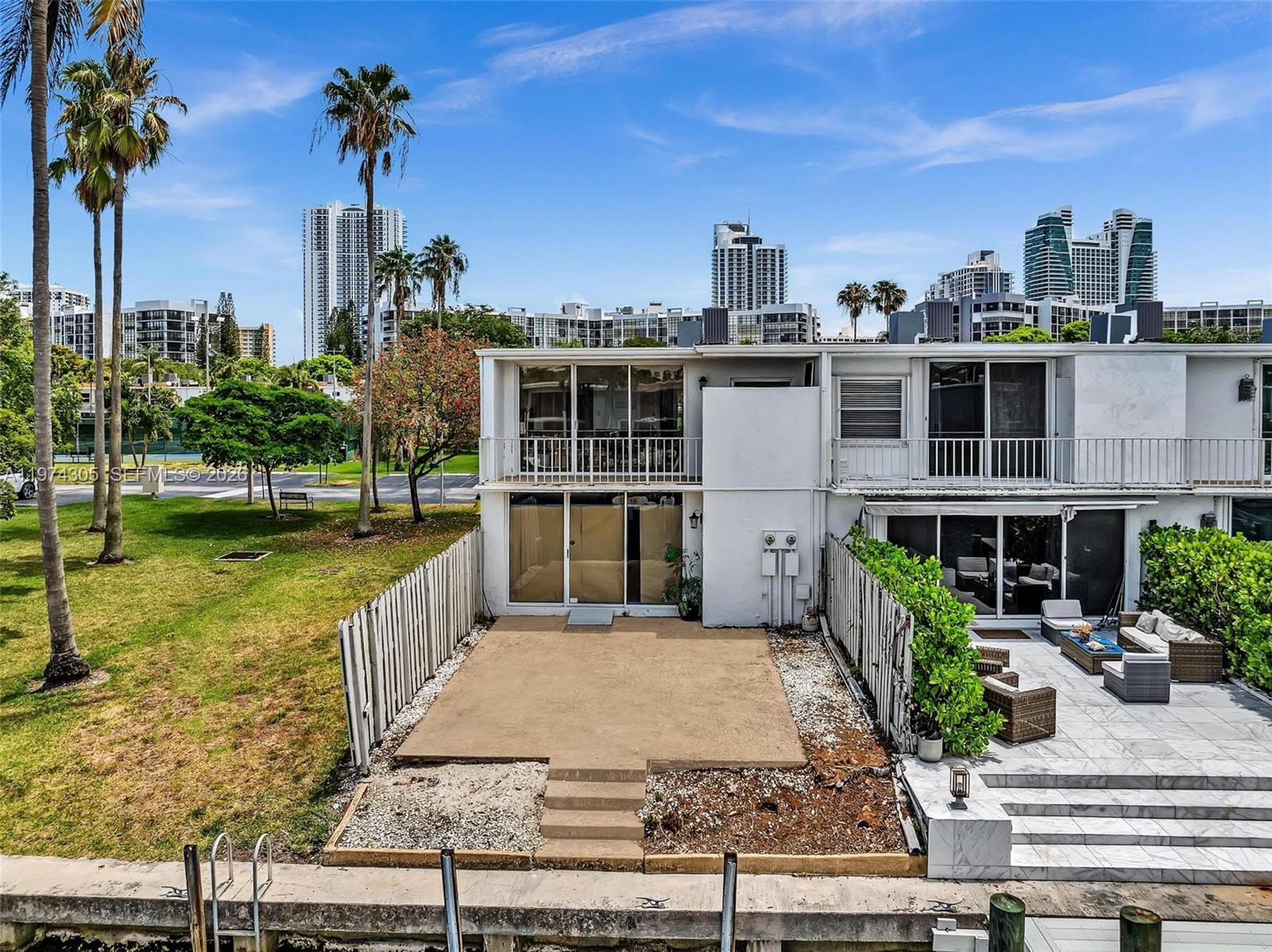 An exterior view of a two-story townhouse with a patio, balcony, and waterfront bulkhead — 825 NE 26th Ave, Hallandale Beach FL 33009, HALLANDALE BEACH, FL