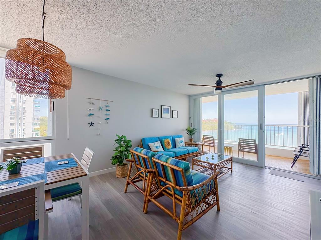 A living and dining area features rattan furniture, blue cushions, and a balcony with ocean views — 200 MARINA VW AVE. UNIT 1910, FAJARDO, PR