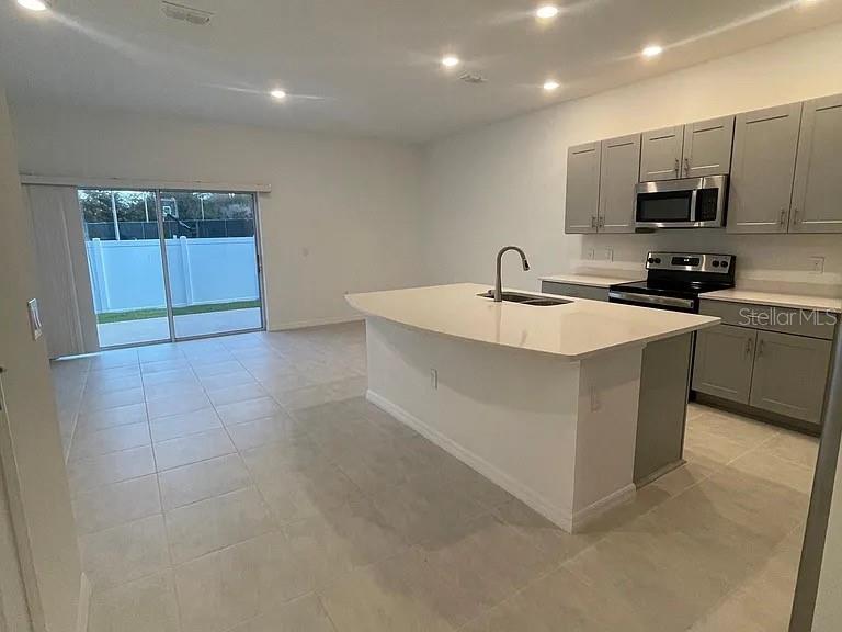 A kitchen with a central island and gray cabinets opens to a tiled living area — 3579 LANDING NET DRIVE, KISSIMMEE, FL