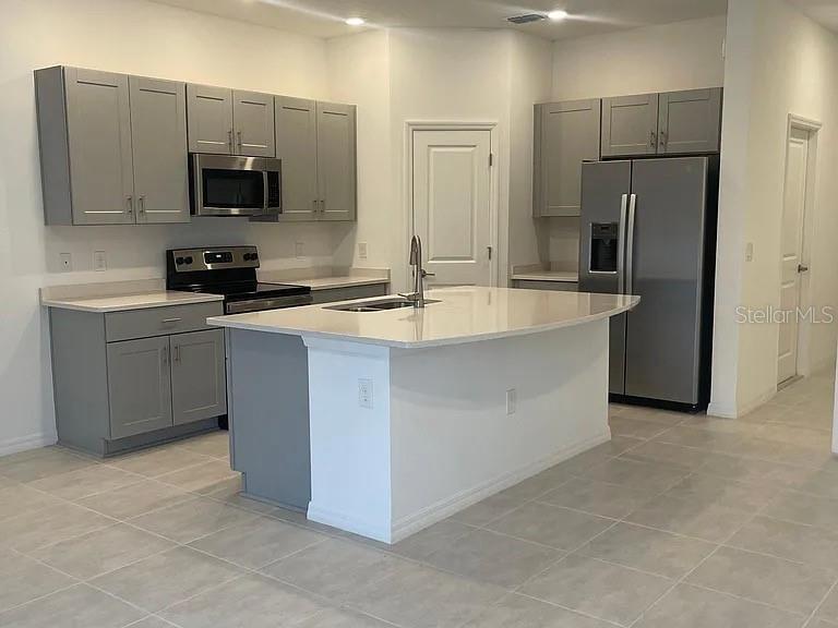 A modern kitchen features gray cabinets, stainless steel appliances, and a central white island — 3579 LANDING NET DRIVE, KISSIMMEE, FL