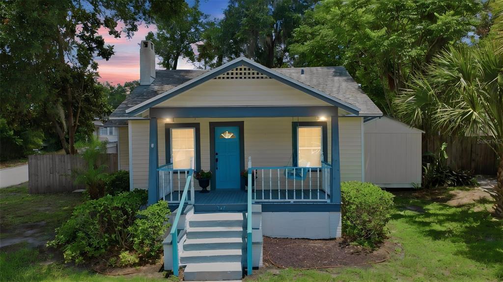 A small, light-yellow bungalow features a blue front door, a covered porch, and a chimney — 347 W WISCONSIN AVENUE, DELAND, FL