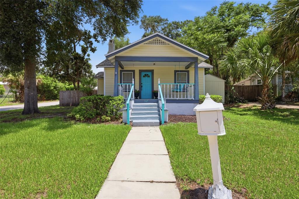 A yellow bungalow with a blue front door and a covered porch sits behind a walkway — 347 W WISCONSIN AVENUE, DELAND, FL