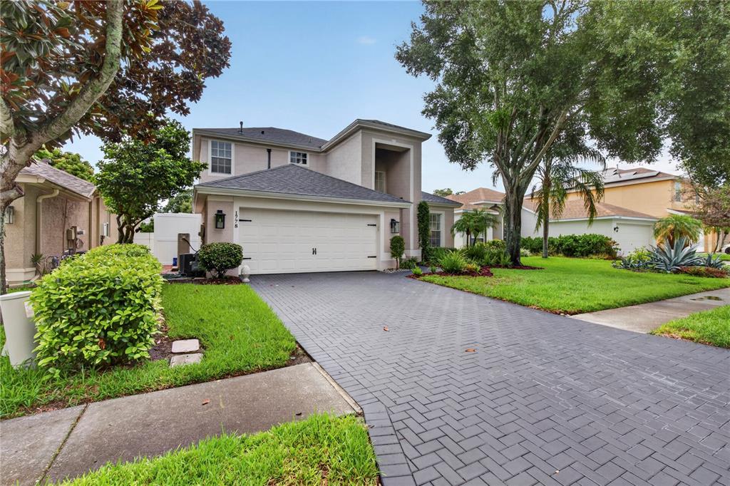 A two-story house features a white garage, a herringbone-patterned driveway, and mature landscaping — 1778 BRILAND STREET, TARPON SPRINGS, FL