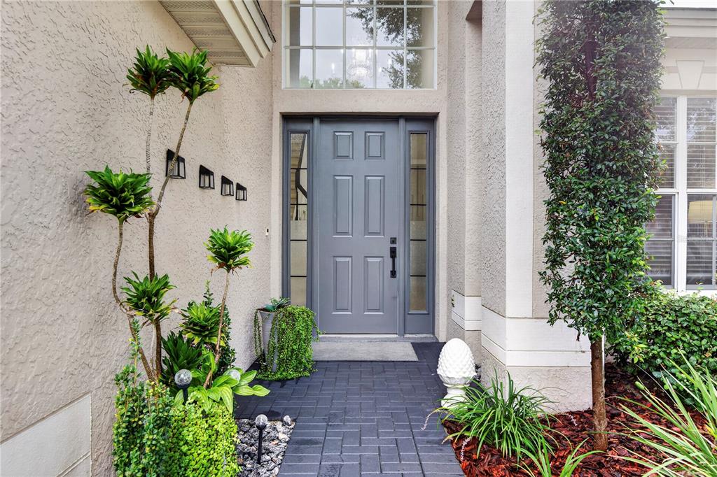 A gray front door with sidelights is framed by a paved walkway and landscaping — 1778 BRILAND STREET, TARPON SPRINGS, FL