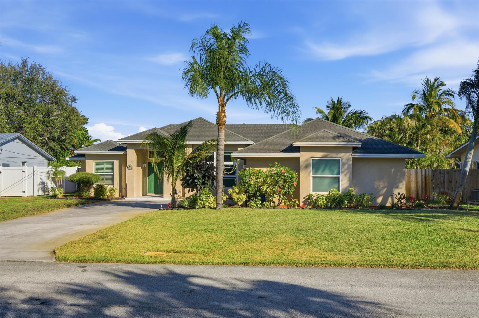 A single-story tan house with a green front door, palm trees, and a concrete driveway — 1569 NE Amy Avenue, Jensen Beach FL 34957, JENSEN BEACH, FL