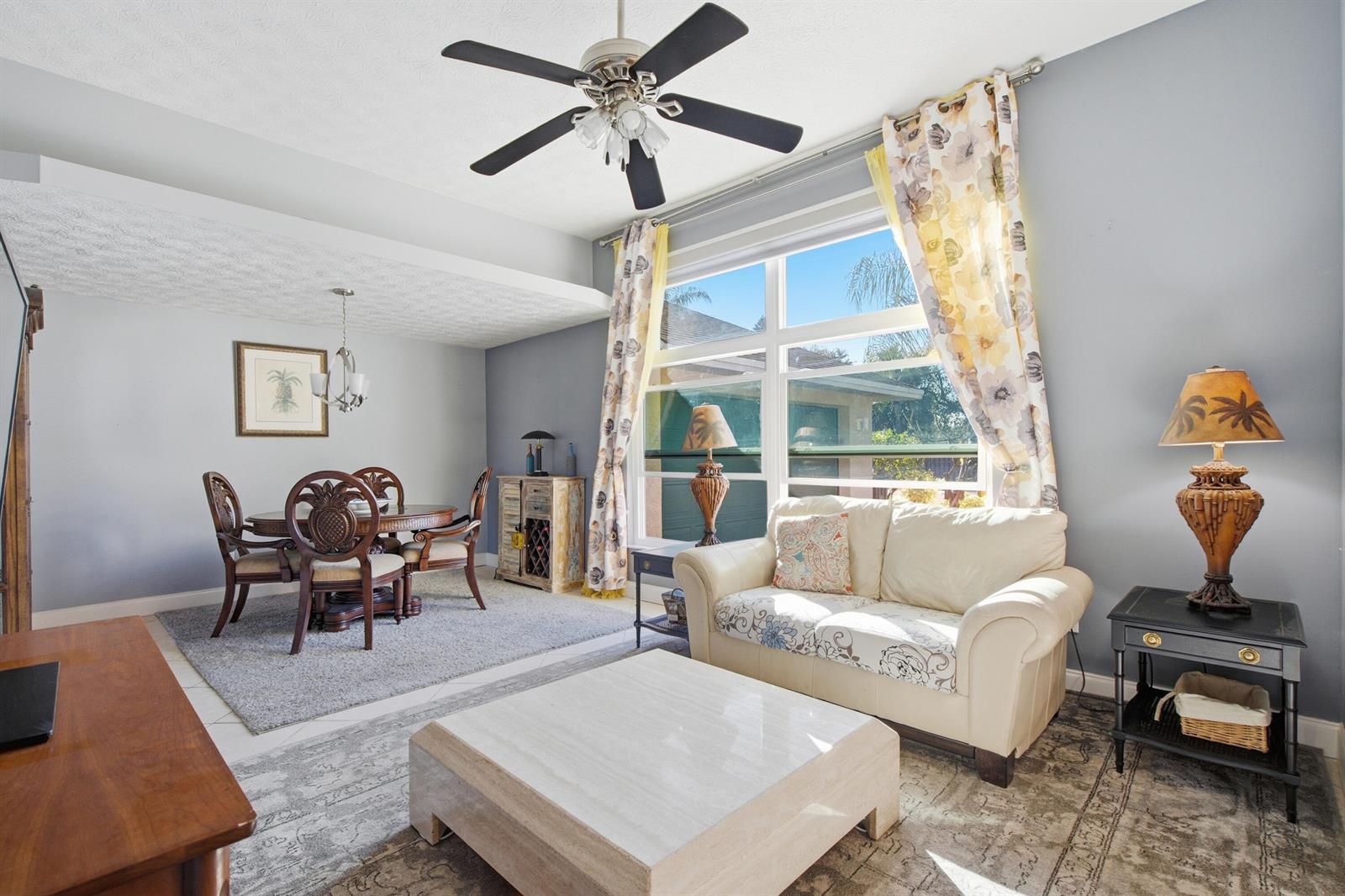A living and dining room features a ceiling fan, large window, and light-colored furniture — 1569 NE Amy Avenue, Jensen Beach FL 34957, JENSEN BEACH, FL