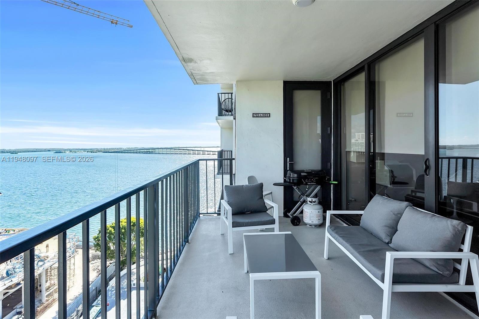 A balcony with outdoor furniture and a grill overlooks a large body of water — 1865 BRICKELL AVENUE # A1501, Miami FL 33129, MIAMI, FL