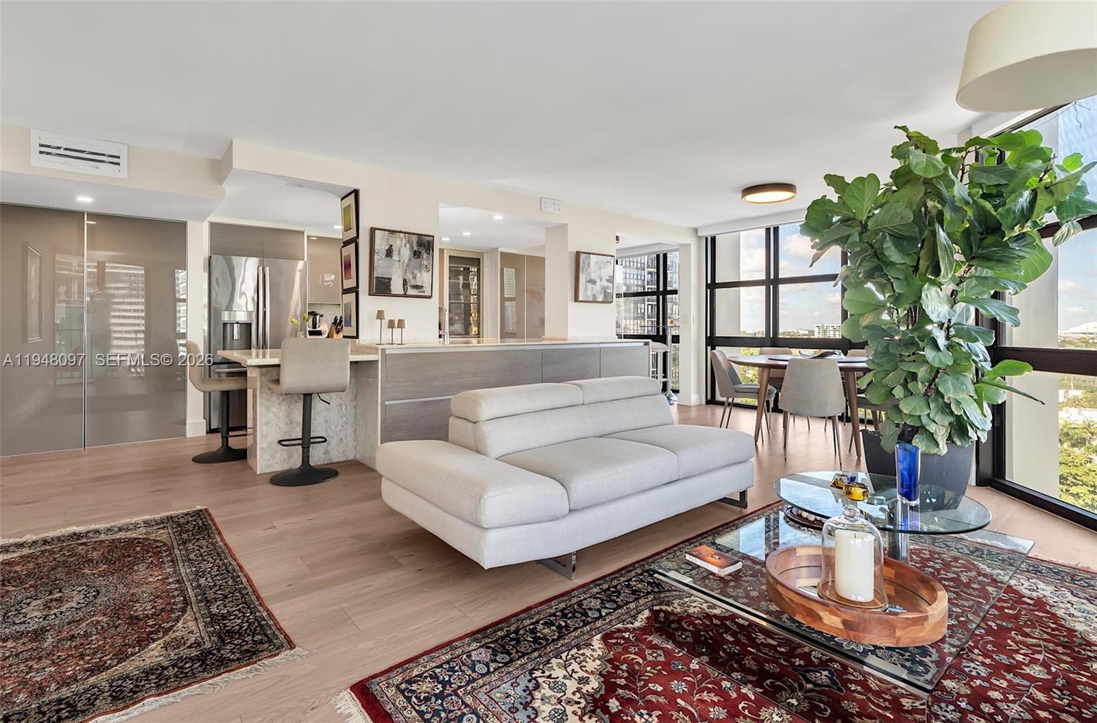 An open-concept living and dining area features a modern kitchen, light wood floors, and rugs — 1865 BRICKELL AVENUE # A1501, Miami FL 33129, MIAMI, FL
