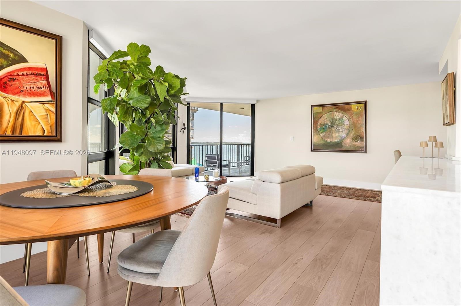 A dining area and living room feature light wood flooring, a large plant, and balcony views — 1865 BRICKELL AVENUE # A1501, Miami FL 33129, MIAMI, FL