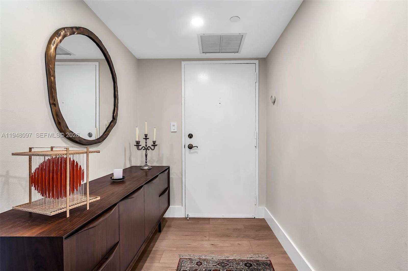 An entryway features a dark wood console table, a round mirror, and a white door — 1865 BRICKELL AVENUE # A1501, Miami FL 33129, MIAMI, FL