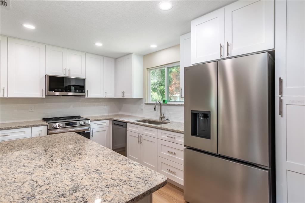 A kitchen features white cabinets, granite countertops, stainless steel appliances, and a subway tile backsplash — 10886 SW 90TH TERRACE, OCALA, FL