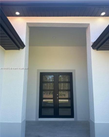 A modern front entryway features double glass doors under a covered porch with recessed lighting — 2002 E 13th St, Lehigh Acres FL 33972, LEHIGH ACRES, FL