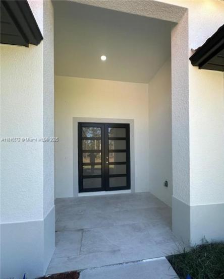 A covered entryway features light-colored tile flooring and a modern black double door — 2002 E 13th St, Lehigh Acres FL 33972, LEHIGH ACRES, FL
