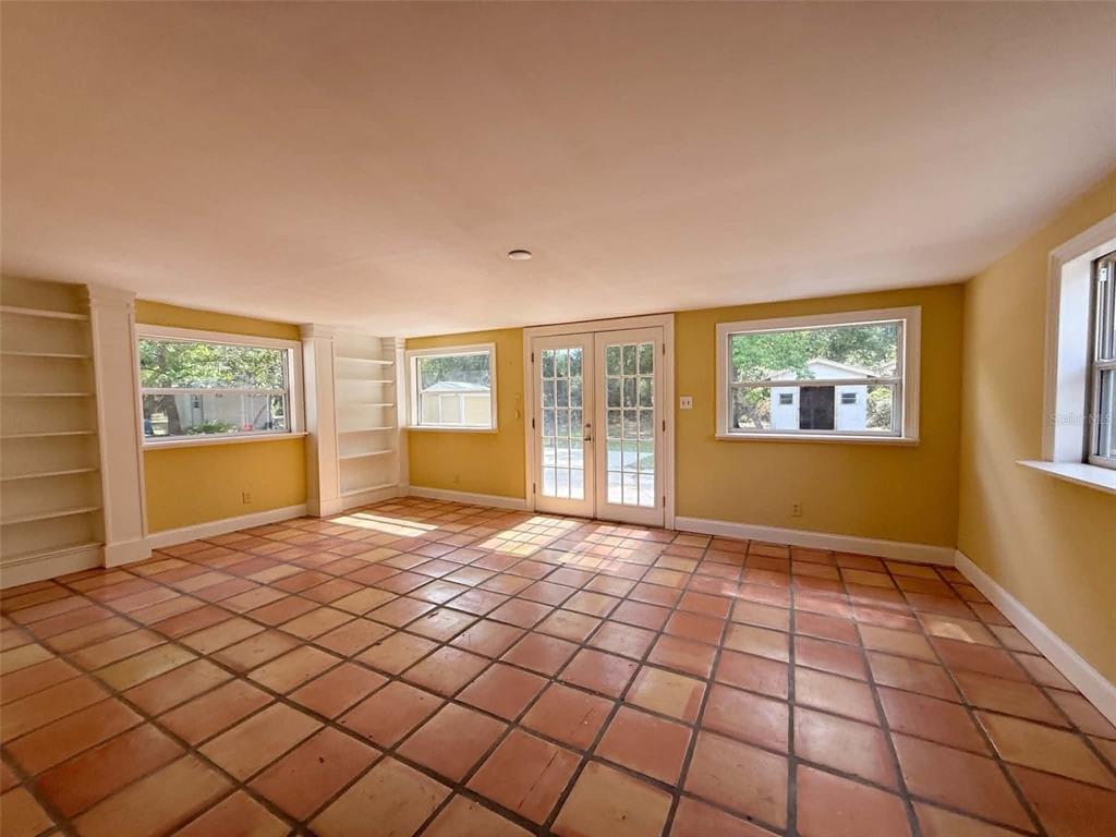 A sunroom with yellow walls, terracotta tile flooring, built-in shelving, and French doors — 11050 NW 107TH TERRACE, CHIEFLAND, FL