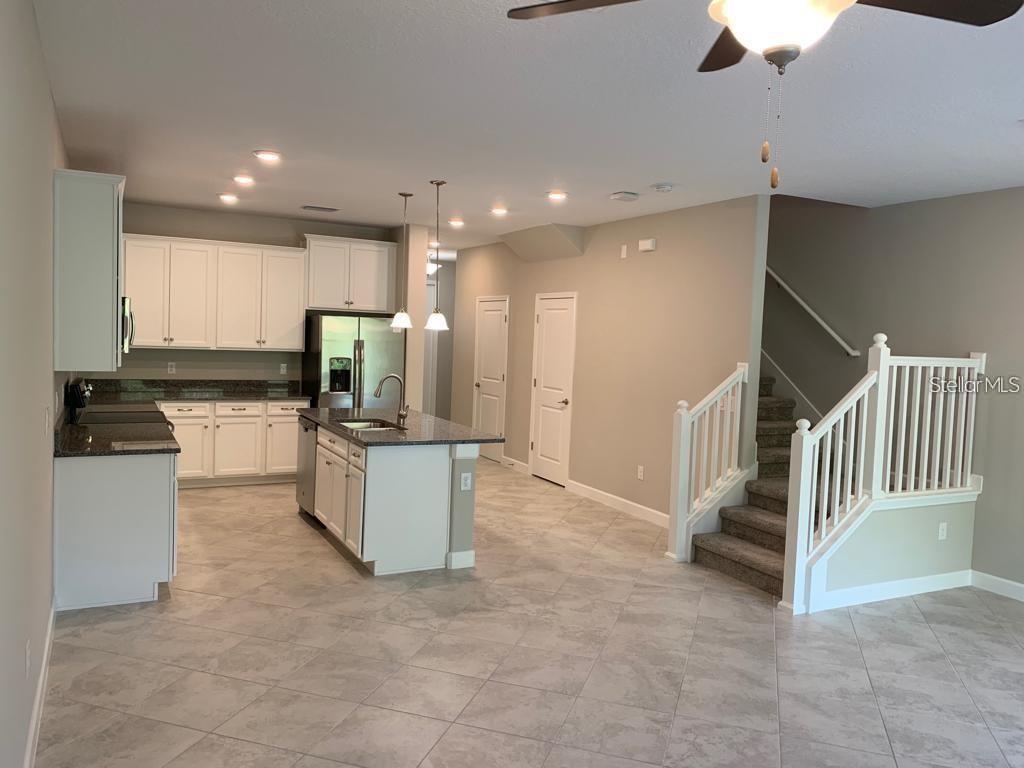 A kitchen with white cabinets and a granite island opens to a carpeted staircase — 18843 NOBLE CASPIAN DRIVE, LUTZ, FL