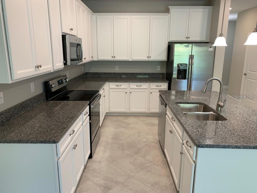 A kitchen with white cabinets, granite countertops, stainless steel appliances, and light-colored tile flooring — 18843 NOBLE CASPIAN DRIVE, LUTZ, FL