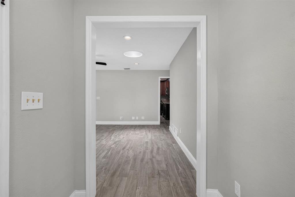 A view through a doorway into a room with gray walls and wood-look flooring — 1017 E INDIAN OAKS, DAYTONA BEACH, FL