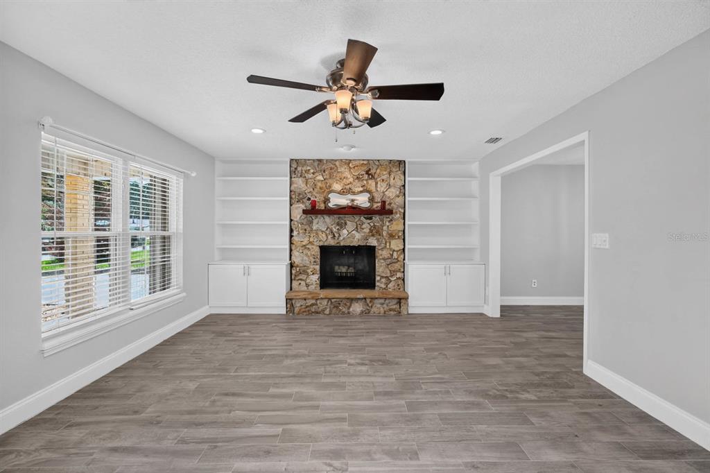 A living room features a stone fireplace, built-in white shelving, and wood-look tile flooring — 1017 E INDIAN OAKS, DAYTONA BEACH, FL