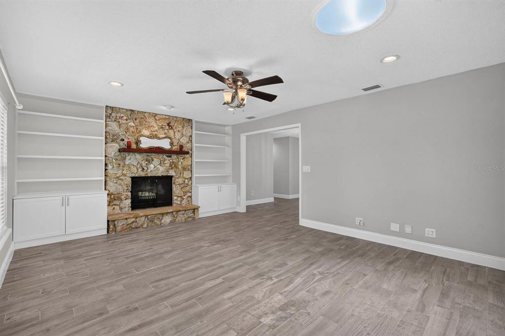 A living room features a stone fireplace, built-in shelving, a ceiling fan, and wood-look flooring — 1017 E INDIAN OAKS, DAYTONA BEACH, FL