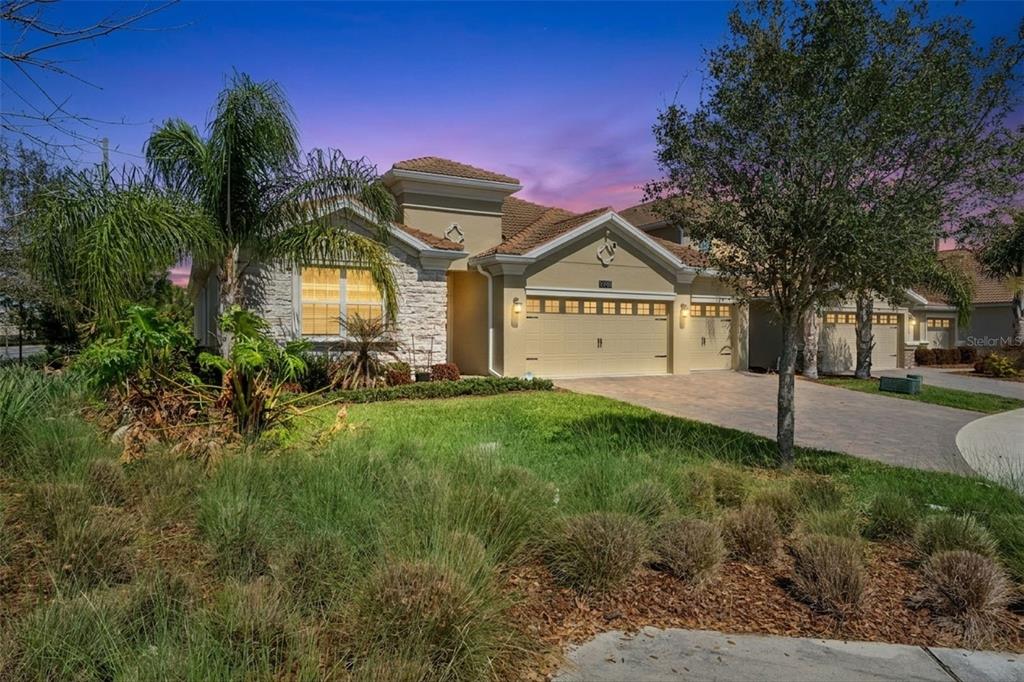 A tan stucco house with a stone facade, a three-car garage, and a landscaped front yard — 8999 CROQUET COURT, DAVENPORT, FL