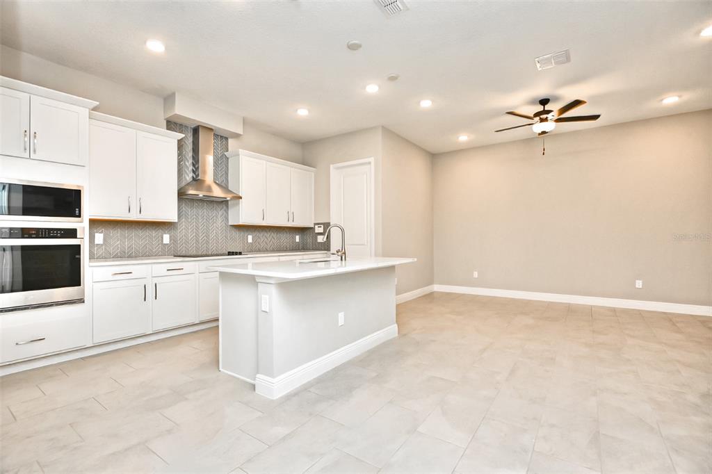 A modern kitchen features white cabinetry, a central island, stainless steel appliances, and tile flooring — 2941 VOYAGER AVENUE, ST CLOUD, FL