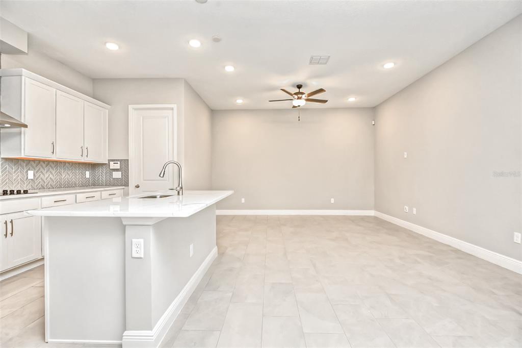 A modern kitchen features white cabinets, a quartz island, and light tile flooring — 2941 VOYAGER AVENUE, ST CLOUD, FL