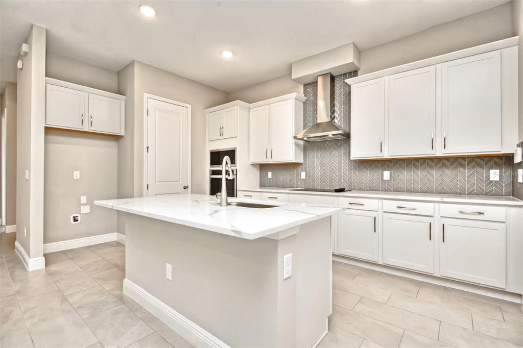 A modern kitchen features white cabinetry, a marble-topped island, and a gray herringbone tile backsplash — 2941 VOYAGER AVENUE, ST CLOUD, FL