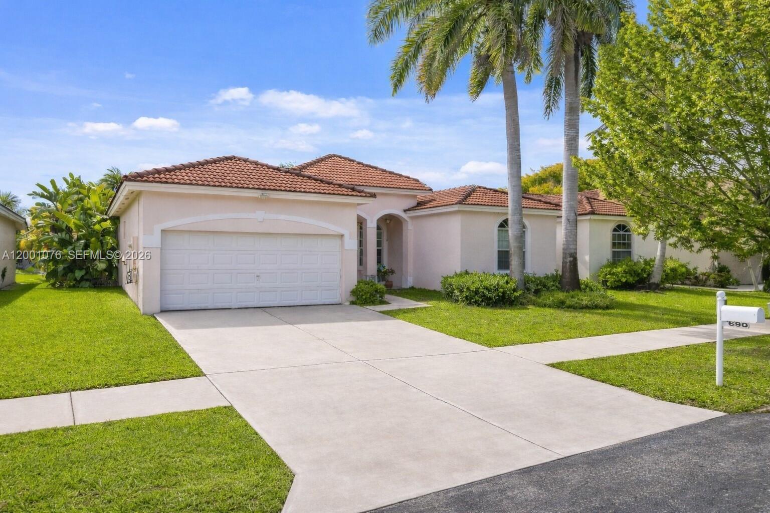 A single-story house with a tile roof, two-car garage, and palm trees in the front yard — 690 SE 30th Dr, Homestead FL 33033, HOMESTEAD, FL