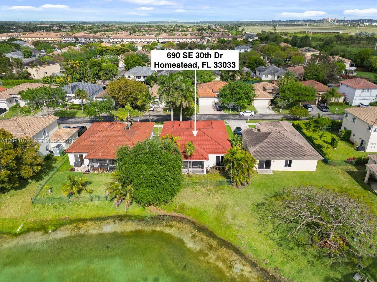 An aerial view shows a residential house with a red tile roof near a pond — 690 SE 30th Dr, Homestead FL 33033, HOMESTEAD, FL