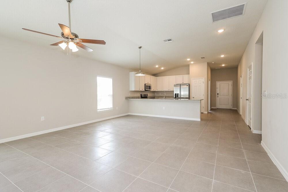 An open-concept kitchen and living area with light tile flooring and white cabinetry — 1660 REDFIN DRIVE, POINCIANA, FL