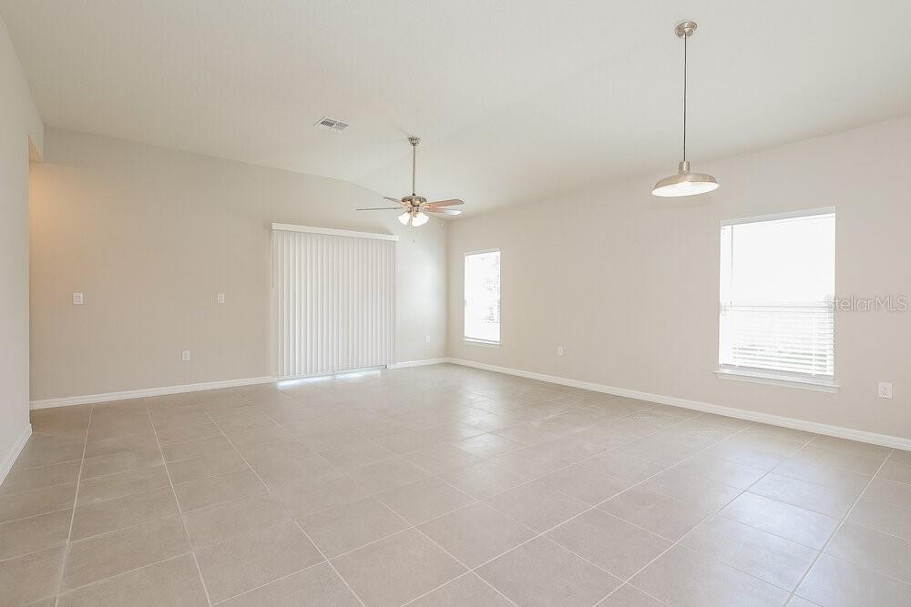 An empty living room with light tile flooring, a ceiling fan, and sliding glass doors — 1660 REDFIN DRIVE, POINCIANA, FL
