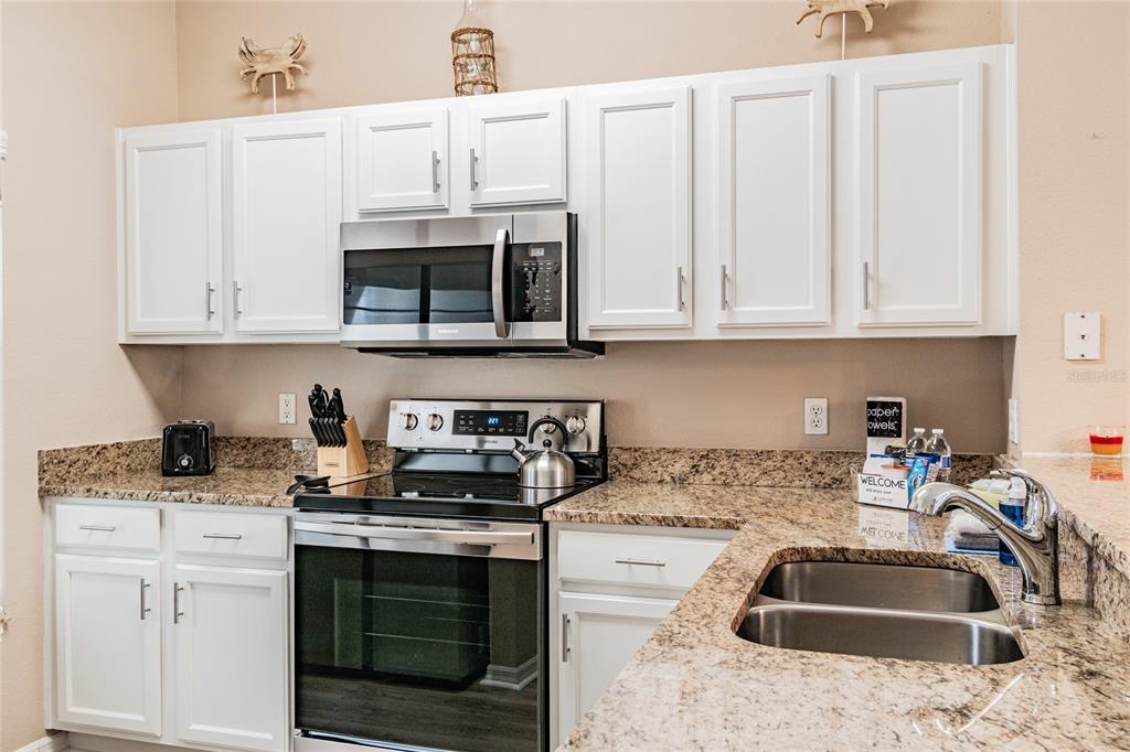 A kitchen features white cabinets, granite countertops, stainless steel appliances, and a double-basin sink — 4504 ALBERTO CIRCLE, KISSIMMEE, FL