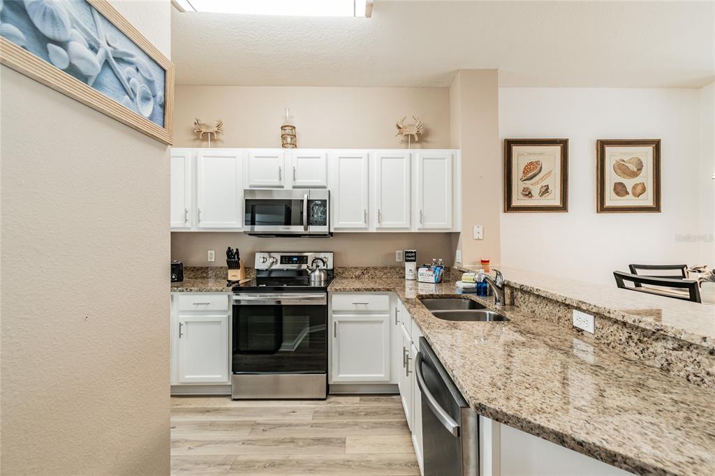 A kitchen features white cabinets, granite countertops, stainless steel appliances, and wood-look flooring — 4504 ALBERTO CIRCLE, KISSIMMEE, FL