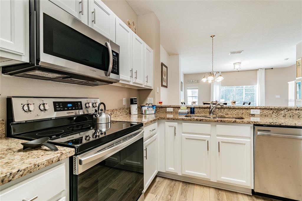 A kitchen features white cabinets, granite countertops, stainless steel appliances, and a view into the dining area — 4504 ALBERTO CIRCLE, KISSIMMEE, FL
