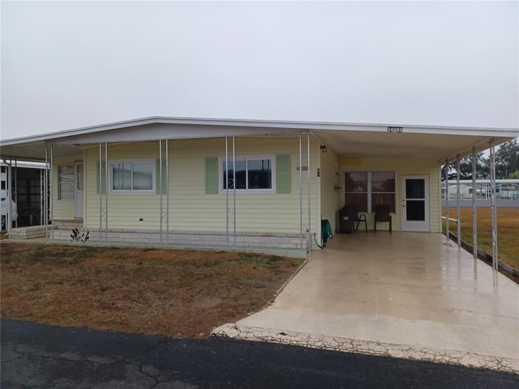 A yellow single-story mobile home features a carport and a covered front porch area — 34604 PETUNIA PLACE, ZEPHYRHILLS, FL