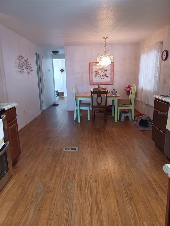 A dining area with a chandelier, wooden table, and light-colored chairs sits on wood-look flooring — 34604 PETUNIA PLACE, ZEPHYRHILLS, FL
