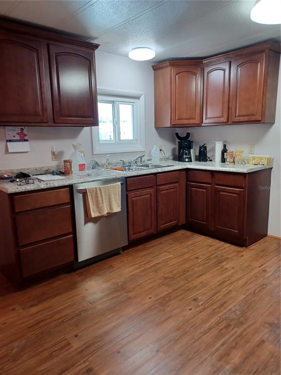 A kitchen features dark wood cabinets, granite-look countertops, stainless steel appliances, and wood-look flooring — 34604 PETUNIA PLACE, ZEPHYRHILLS, FL