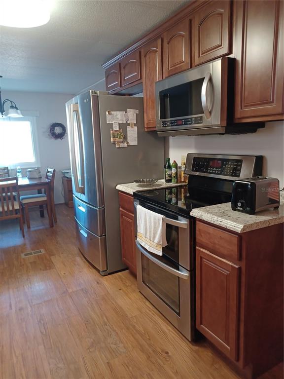 A kitchen with wood cabinets, stainless steel appliances, and a dining area in the background — 34604 PETUNIA PLACE, ZEPHYRHILLS, FL