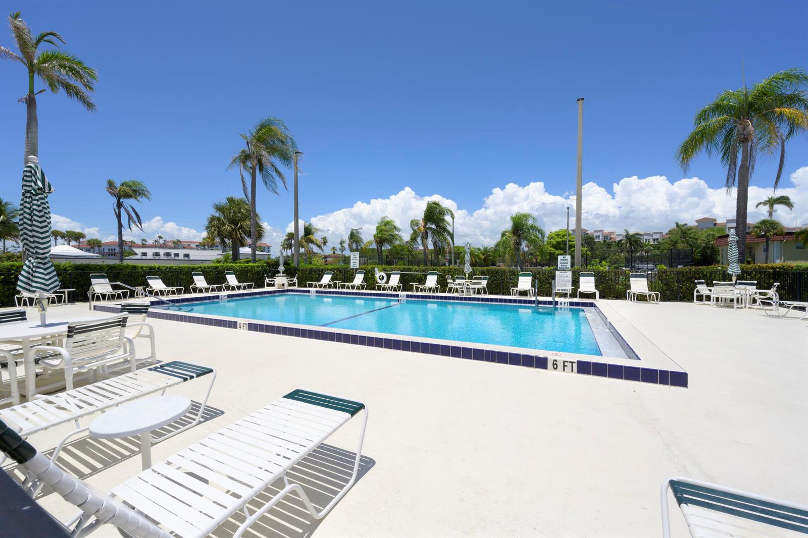 An outdoor swimming pool surrounded by lounge chairs, tables, and palm trees under a blue sky — 717 S Us Highway 1 # 211, Jupiter FL 33477, JUPITER, FL