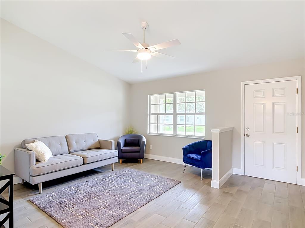A living room features light gray walls, wood-look tile flooring, a ceiling fan, and furniture — 1472 4TH STREET, ORANGE CITY, FL