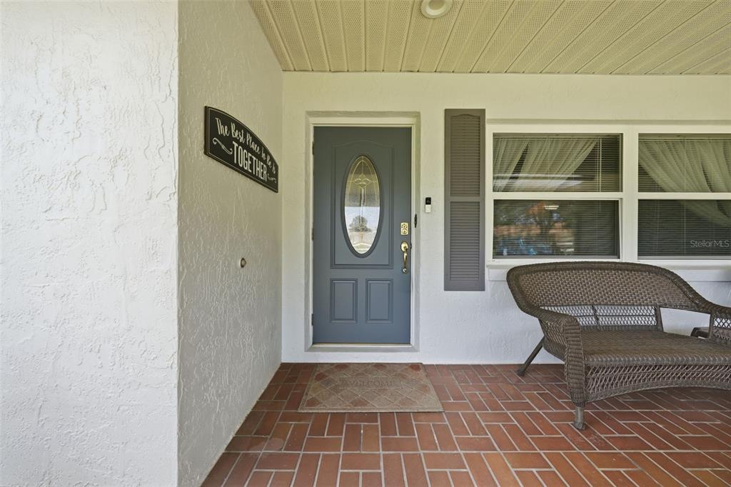 A covered front porch features a grey door, brick flooring, and a wicker bench — 42 S J KELLNER BOULEVARD, BEVERLY HILLS, FL