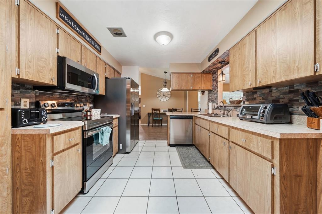A kitchen features wood cabinets, stainless steel appliances, a tiled floor, and a stone backsplash — 42 S J KELLNER BOULEVARD, BEVERLY HILLS, FL
