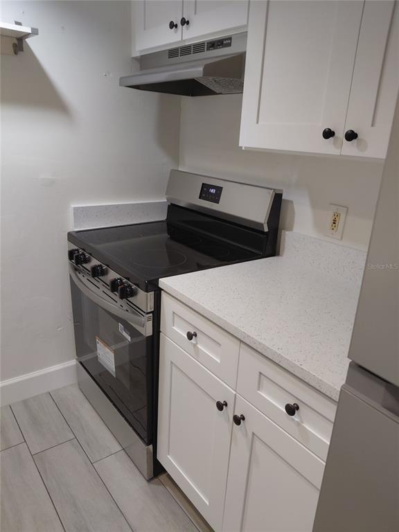 A kitchen features white cabinets, a stainless steel electric stove, and light-colored speckled countertops — 4725 JOSEPH COURT UNIT 229, TAMPA, FL