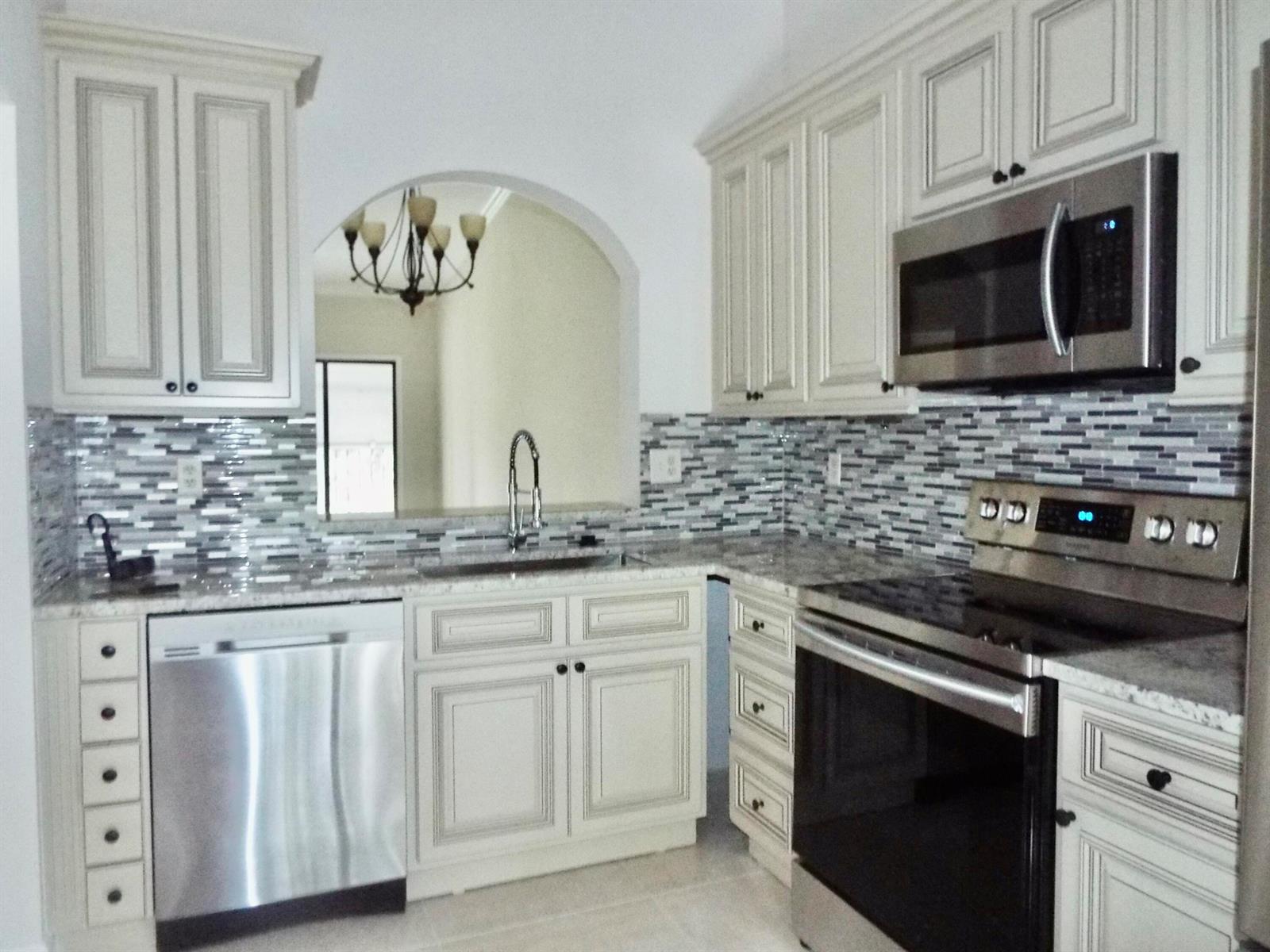 A kitchen features off-white cabinets, stainless steel appliances, and a multi-colored glass tile backsplash — 3350 Perimeter Drive # 1323, FL 33467, FL