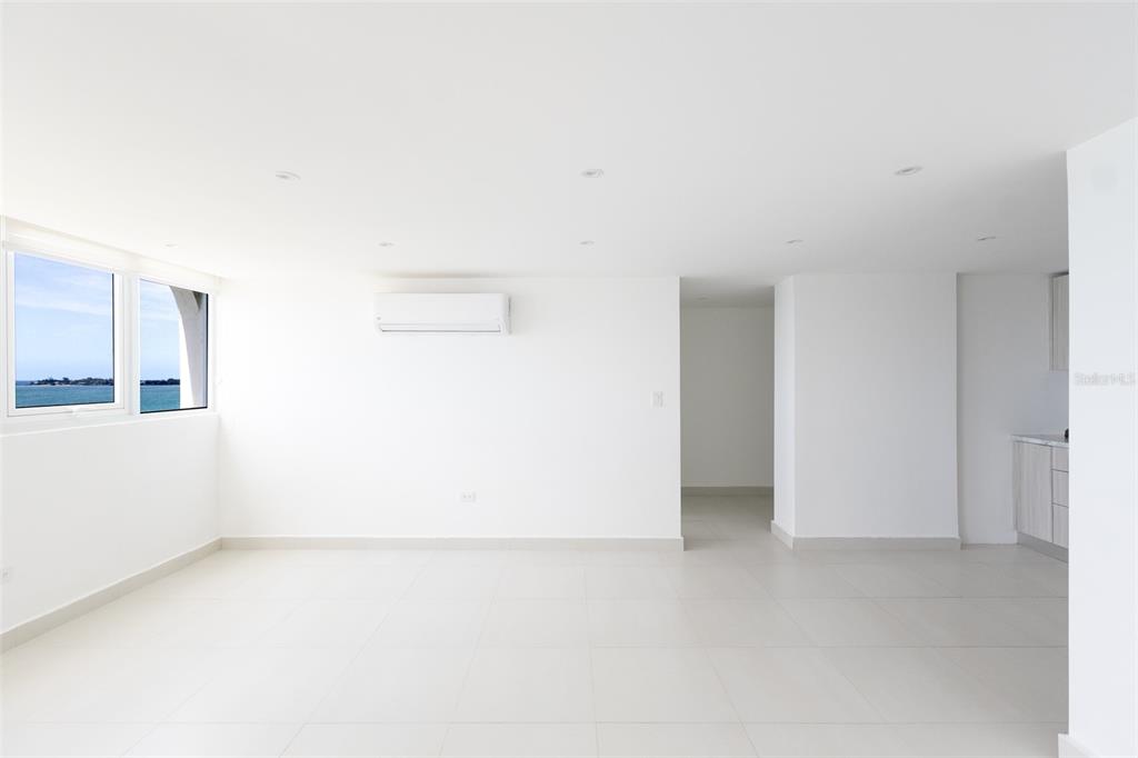 A bright, minimalist room features white tile floors, a wall-mounted air conditioner, and ocean views — PH 807B PLAYA DORADA, CAROLINA, PR