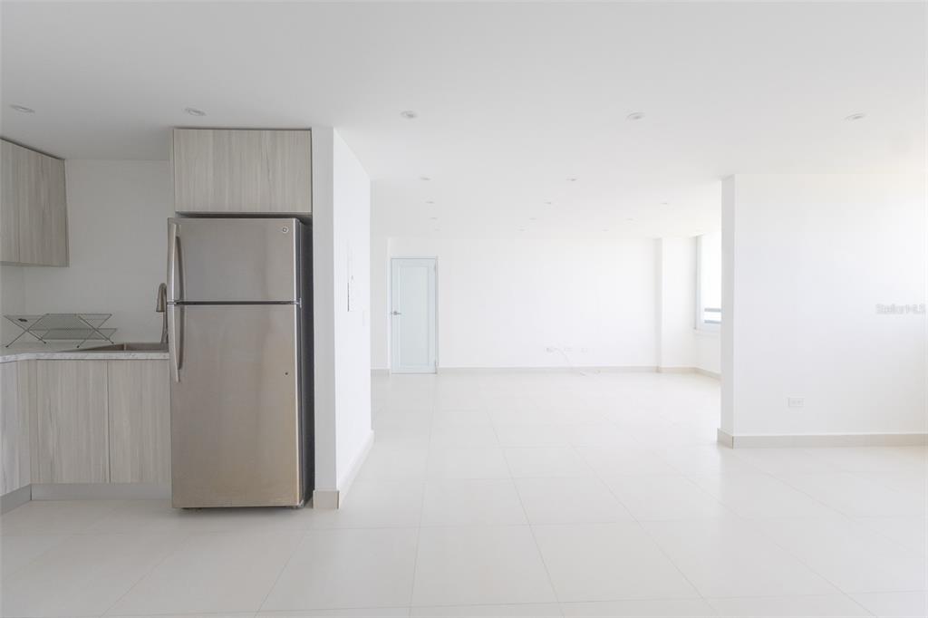 A kitchen with stainless steel appliances and light wood cabinets opens into a white room — PH 807B PLAYA DORADA, CAROLINA, PR